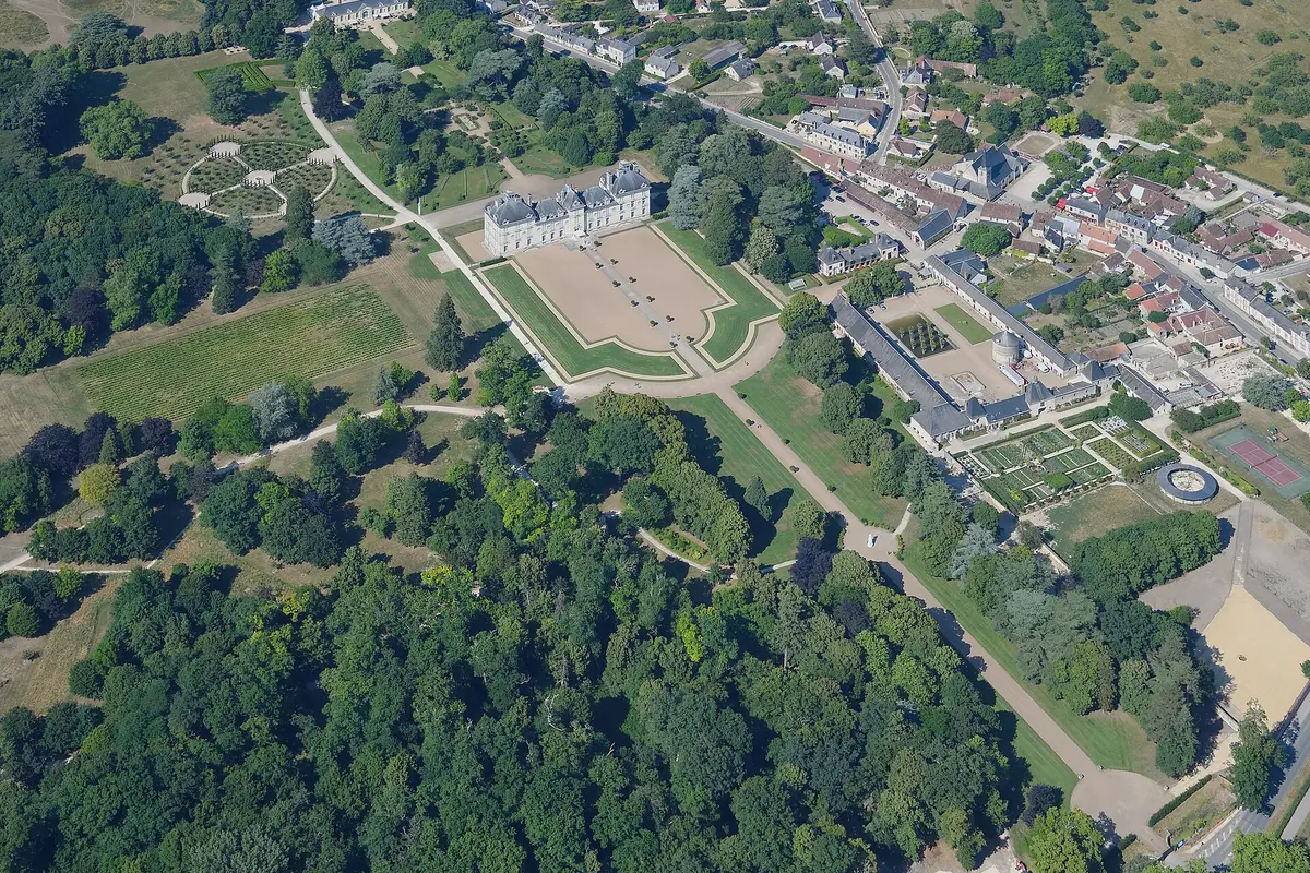 Aerial view of the Château de Cheverny with its formal forecourt, the gardens and outbuildings to the right, the village beyond and woodland in the foreground